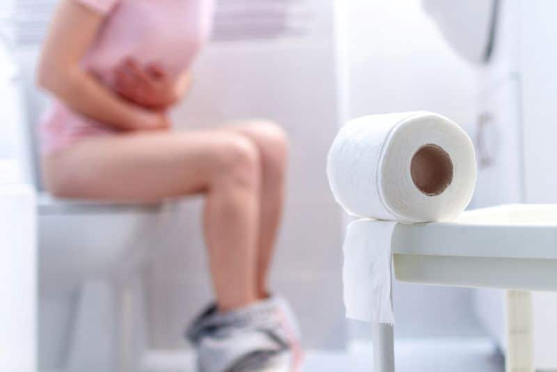 Woman hunched over the toilet with menopause diarrhea
