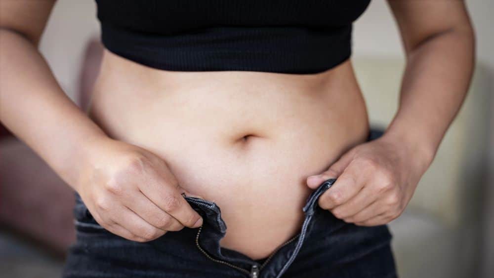 Perimenopause woman struggles to button up her jeans due to bloating