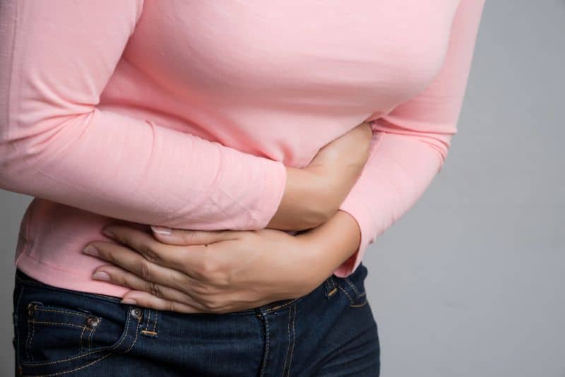 Woman in pink shirt holding her abdomen with menopause bloating pain