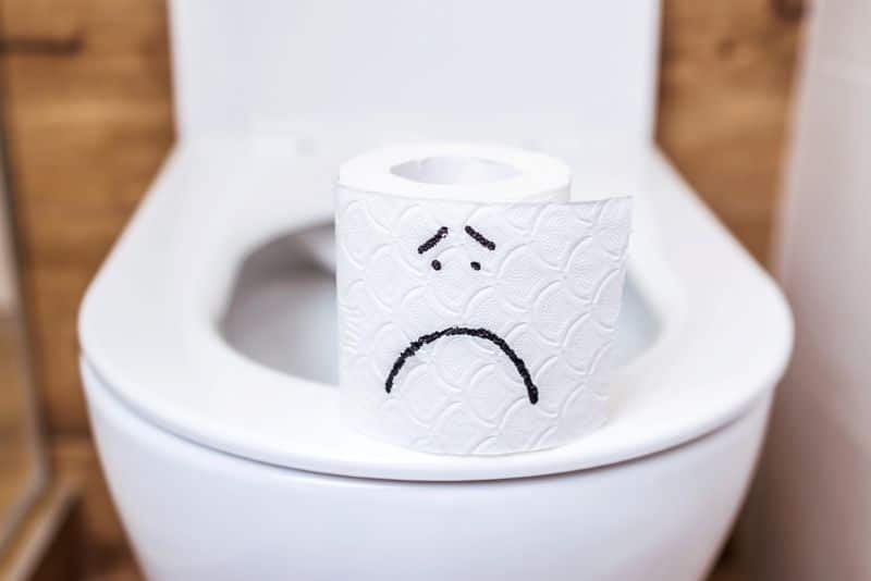 Close-up roll of white toilet paper with a painted sad face stands on the toilet. 