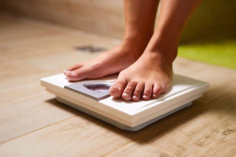 Woman staning on scale weighing the costs of dieting