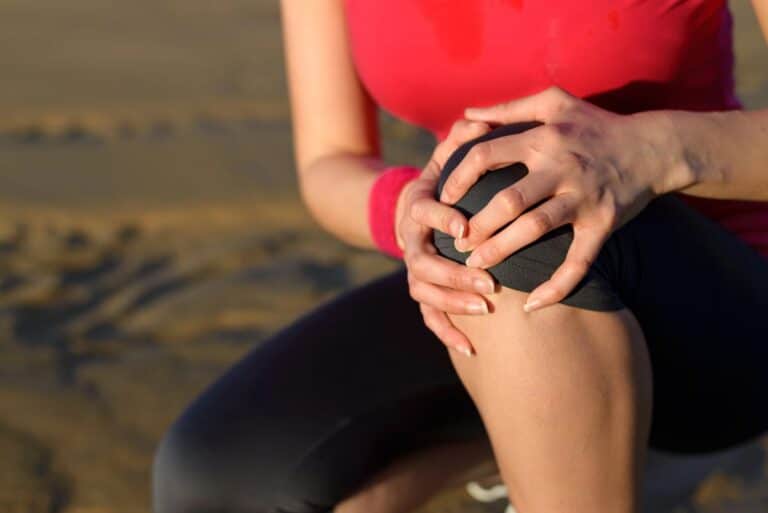 Woman sitting outdoors holding her knee with both hands, suggesting joint discomfort during physical activity. This visual introduces the question “can diet help joint pain in menopause” by highlighting a common symptom.