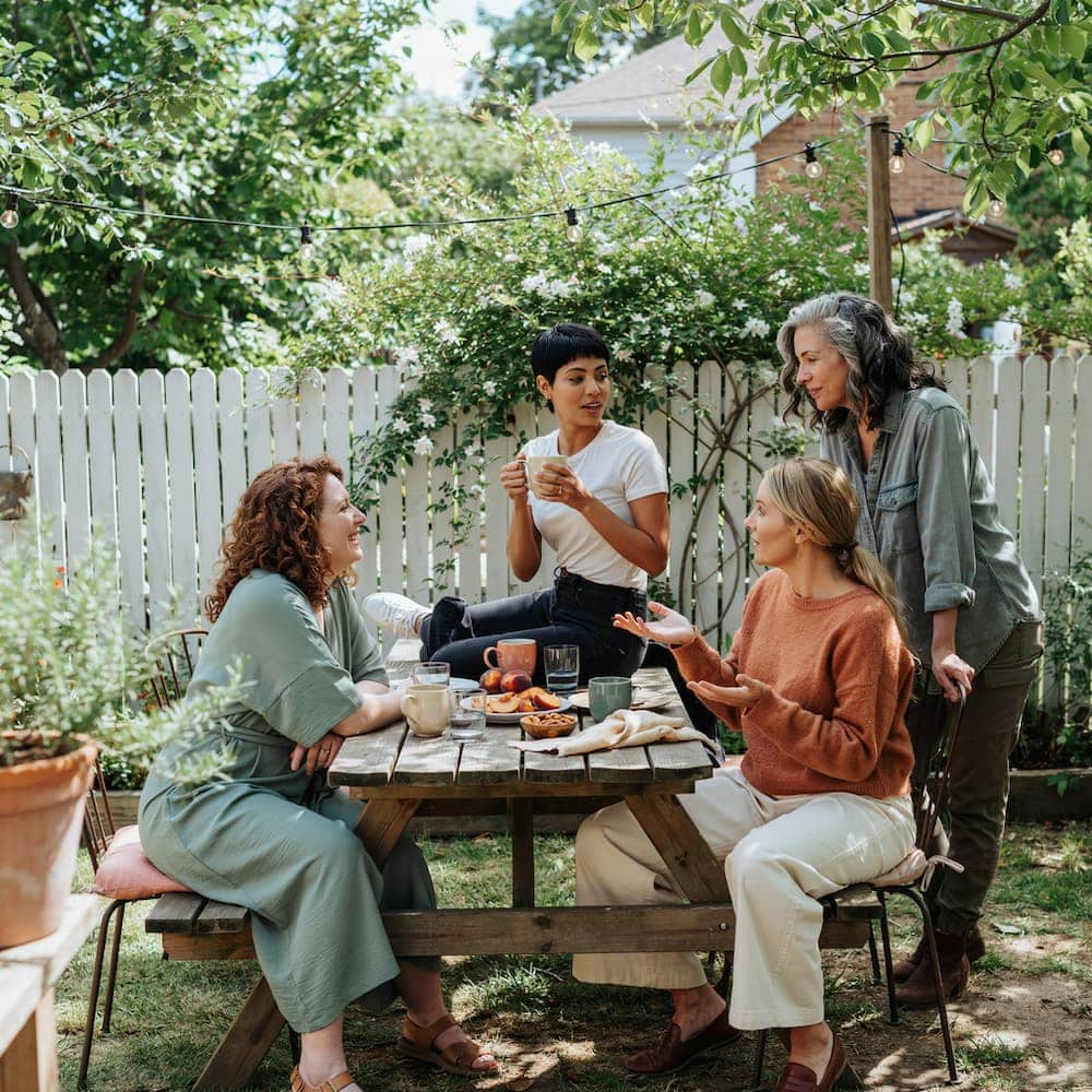 Four midlife women sharing a meal and conversation in a backyard garden